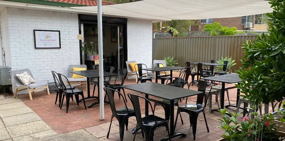 The Loving Hut courtyard with black tables and chairs under a white shade sail