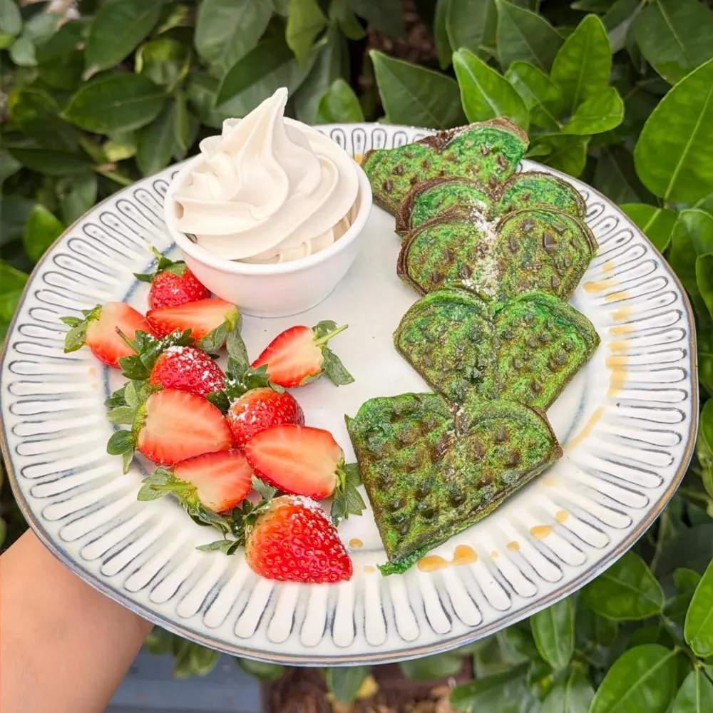 Green heart-shaped coconut pandan waffles with strawberries and soft serve