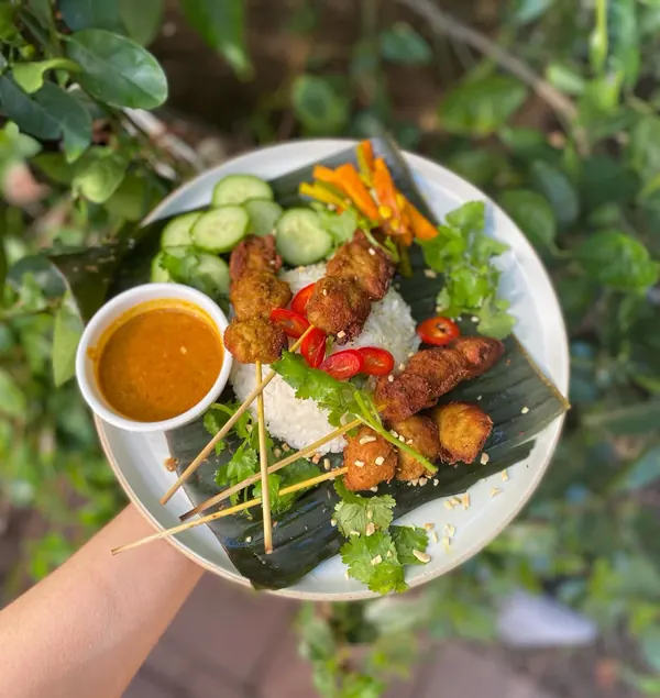 Satay skewers with coconut rice, peanut sauce and pickled vegetables on a banana leaf