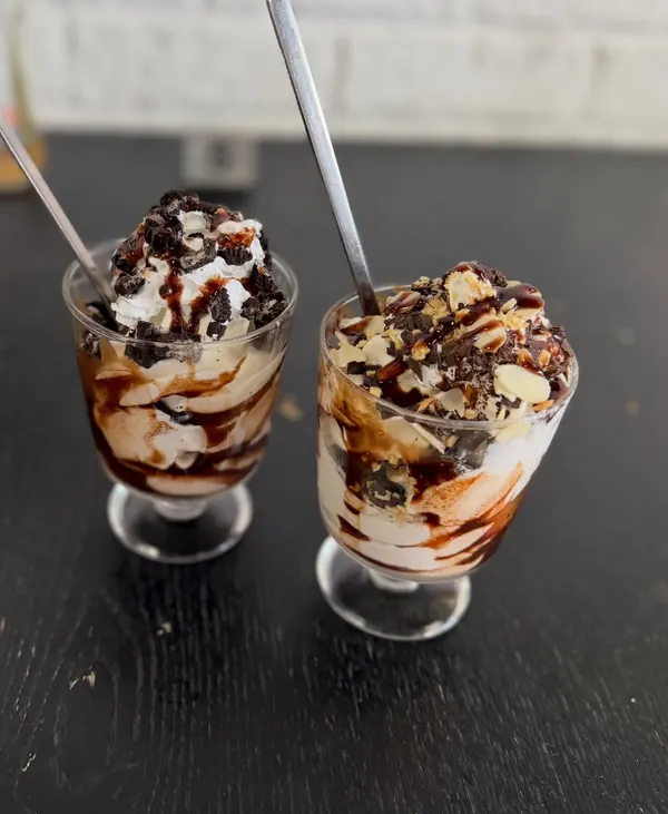 Two soft serve sundaes with chocolate sauce, cookies and almonds